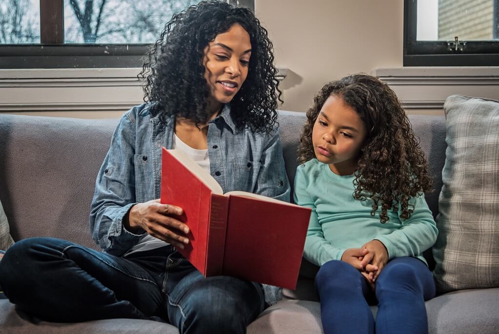 mom reads book to daughter while sitting on couch